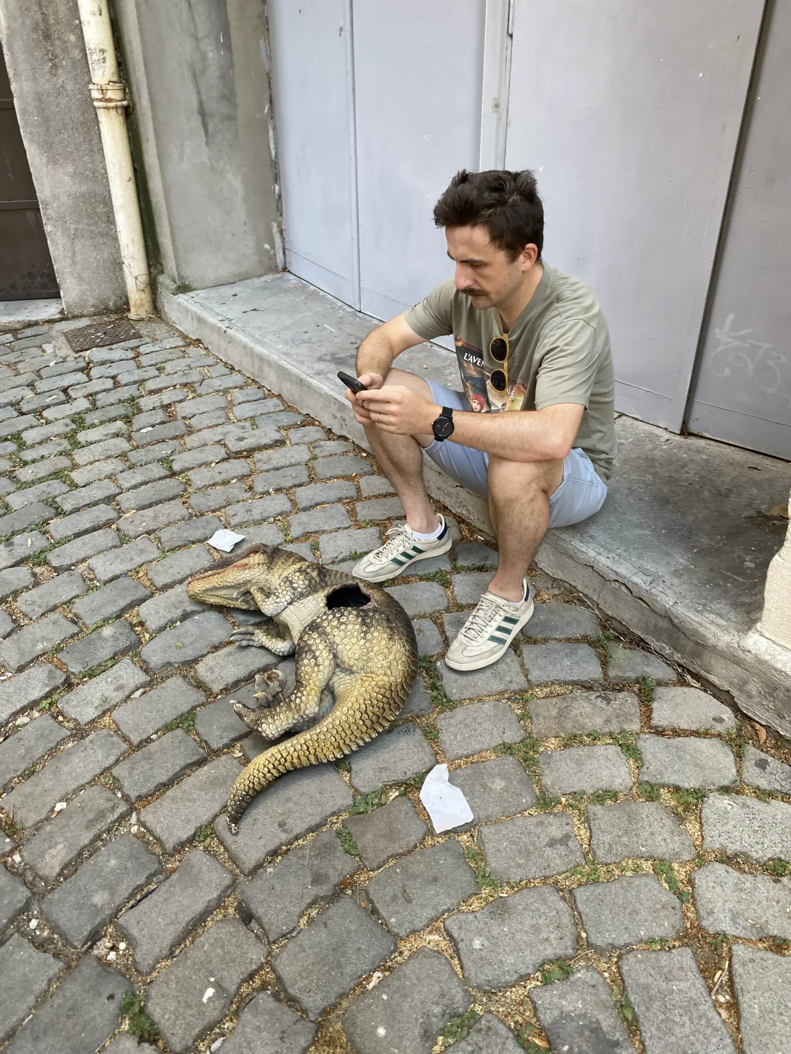 Comédien en pause de tractage face à un vélociraptor desséché.