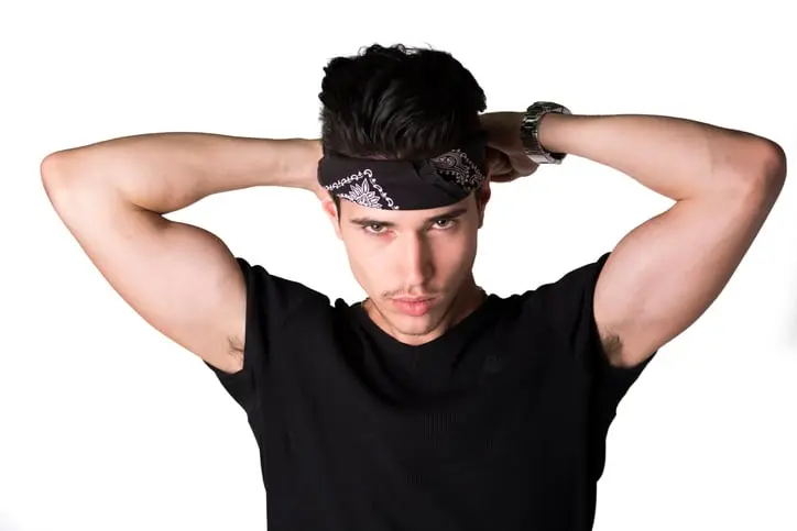 Handsome young man tying headband around head looking at camera, isolated on white